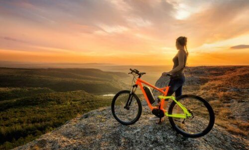 kvinde der står på en bakketop med en cykel